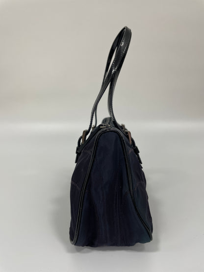 Side view of a Prada Tessuto Spazzolato bag in indigo prune nylon showcasing its slim profile and leather handles.