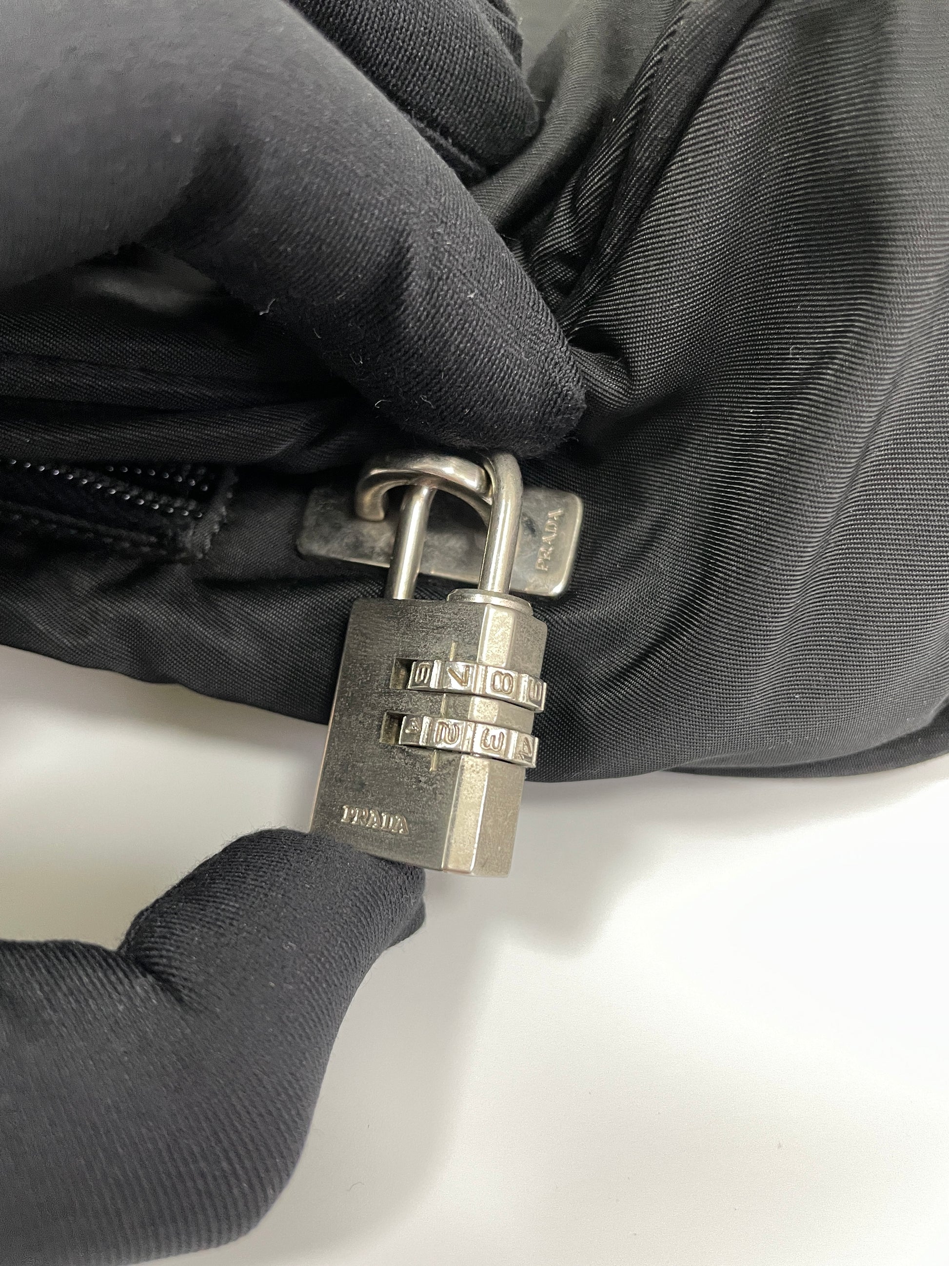 Close-up of the silver combination lock attached to the zipper of the Prada Tessuto Tote Bag in black nylon, adding an extra layer of security.