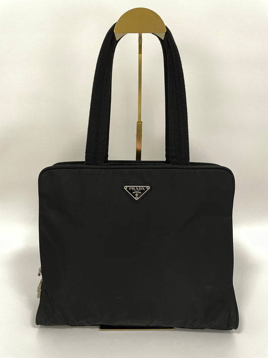 Front view of the Prada Tessuto Tote Bag in black nylon with dual top handles and the signature triangular Prada logo emblem.