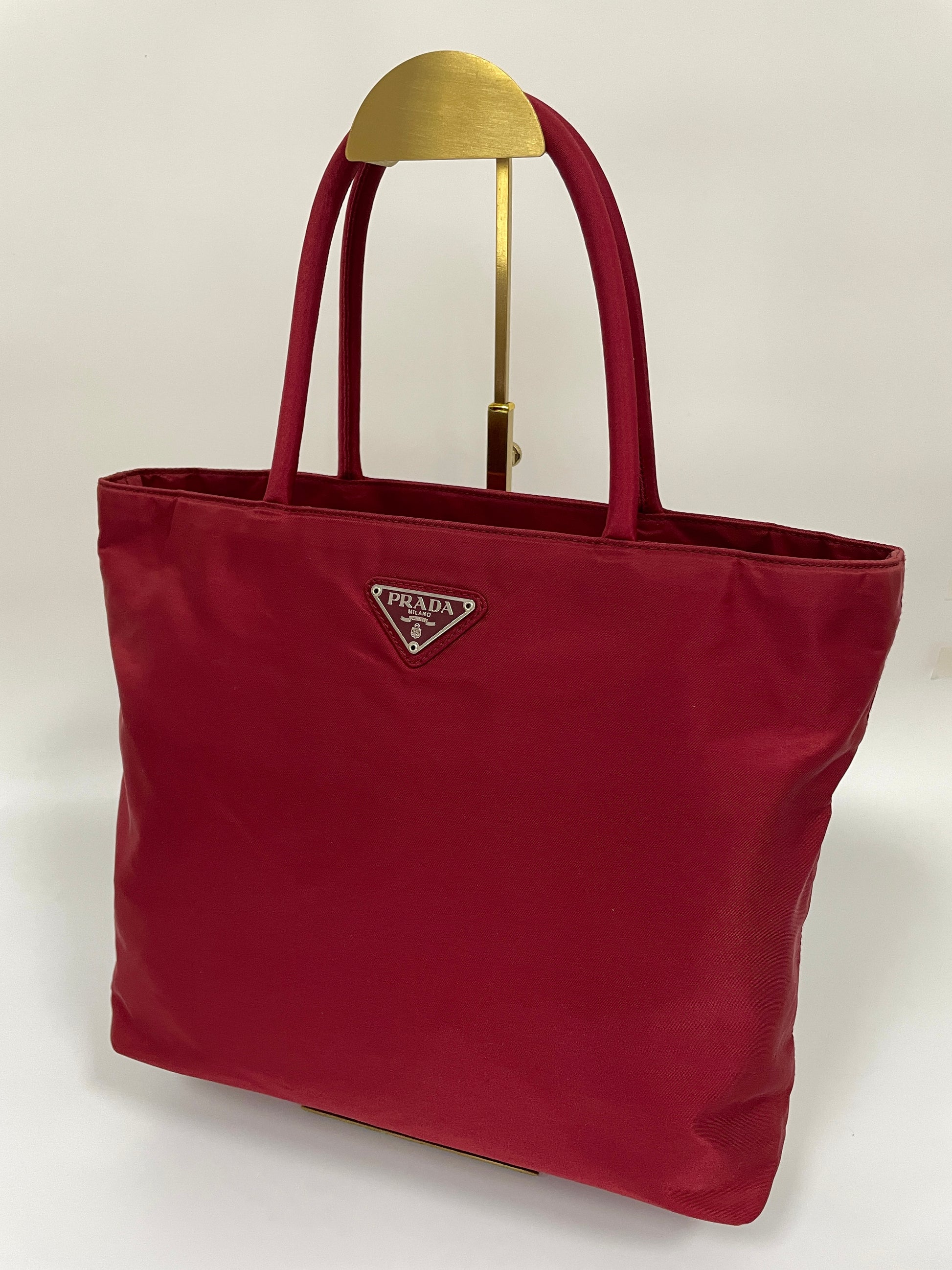 Angled view of a Prada Tessuto Tote Bag in red nylon with dual handles and the Prada triangle logo