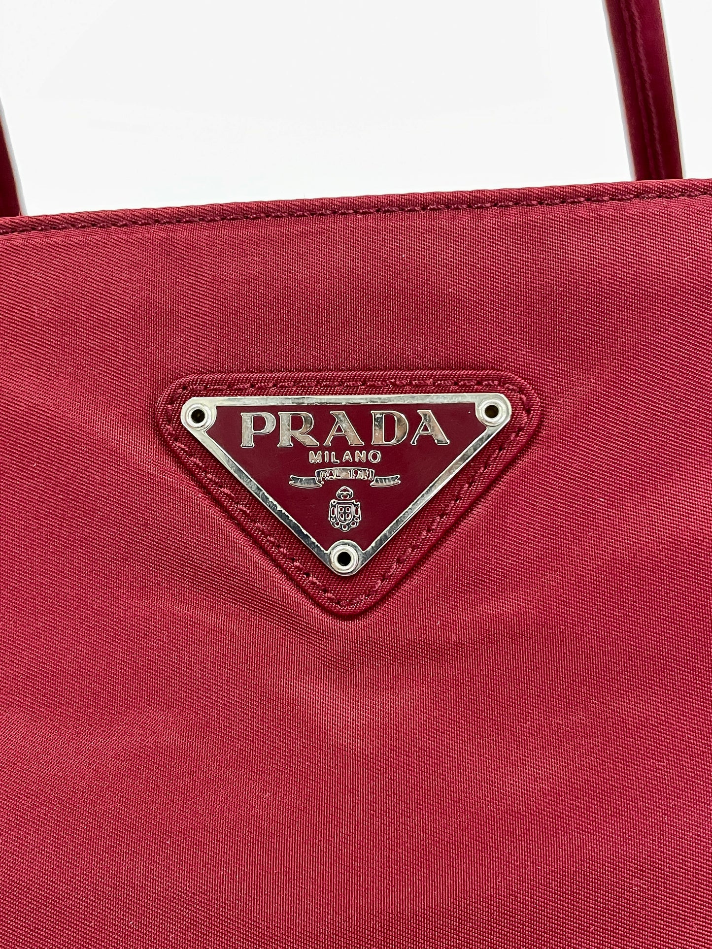 Close-up view of the Prada triangle logo on the Prada Tessuto Tote Bag in red nylon.