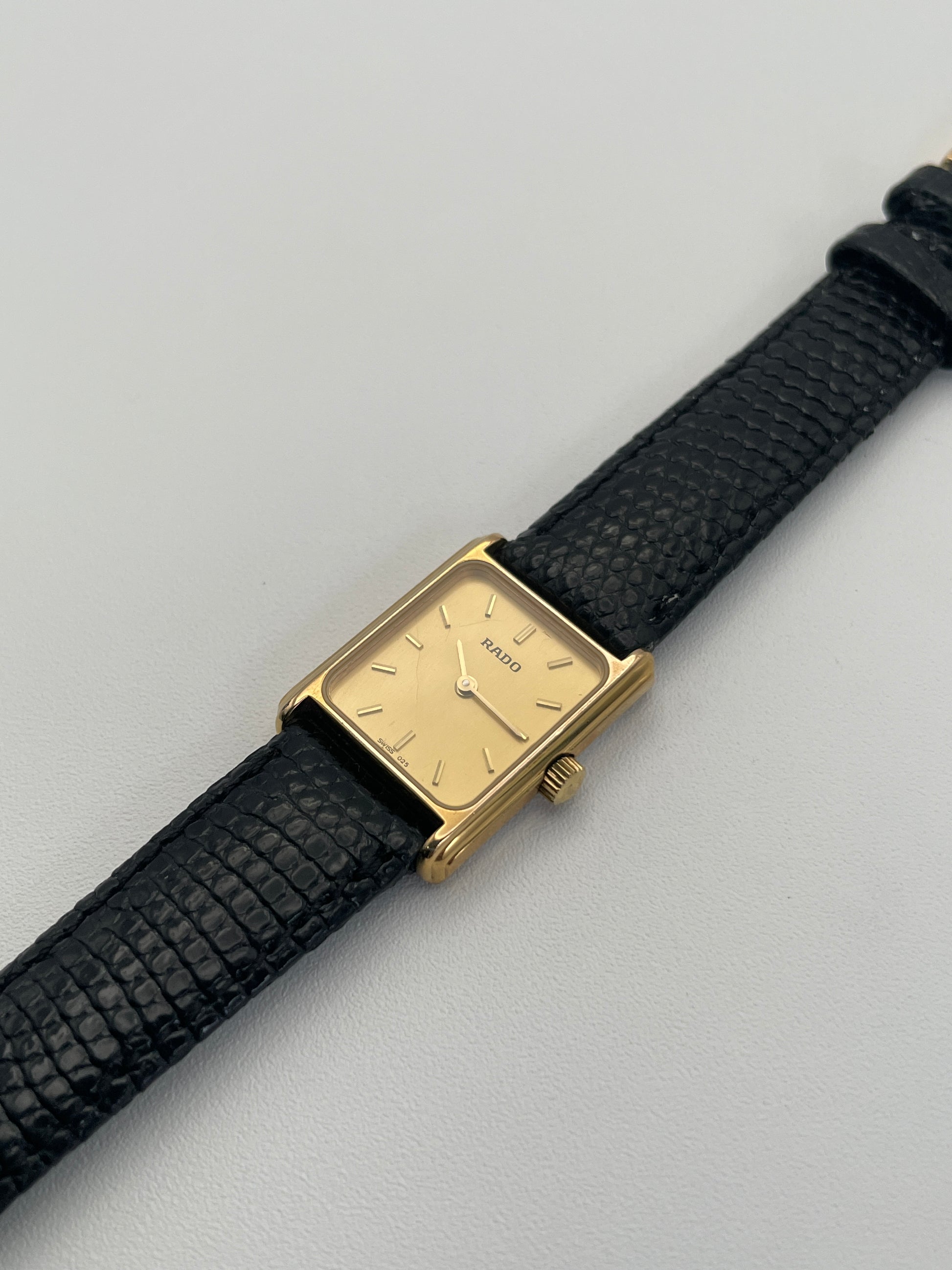 Rado Tank watch in gold case with a rectangular dial and black leather strap, diagonal view.