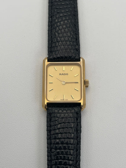 Rado Tank watch in gold case with a rectangular dial and black leather strap, front view.