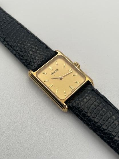 Rado Tank watch in gold case with a rectangular dial and black leather strap, front view.