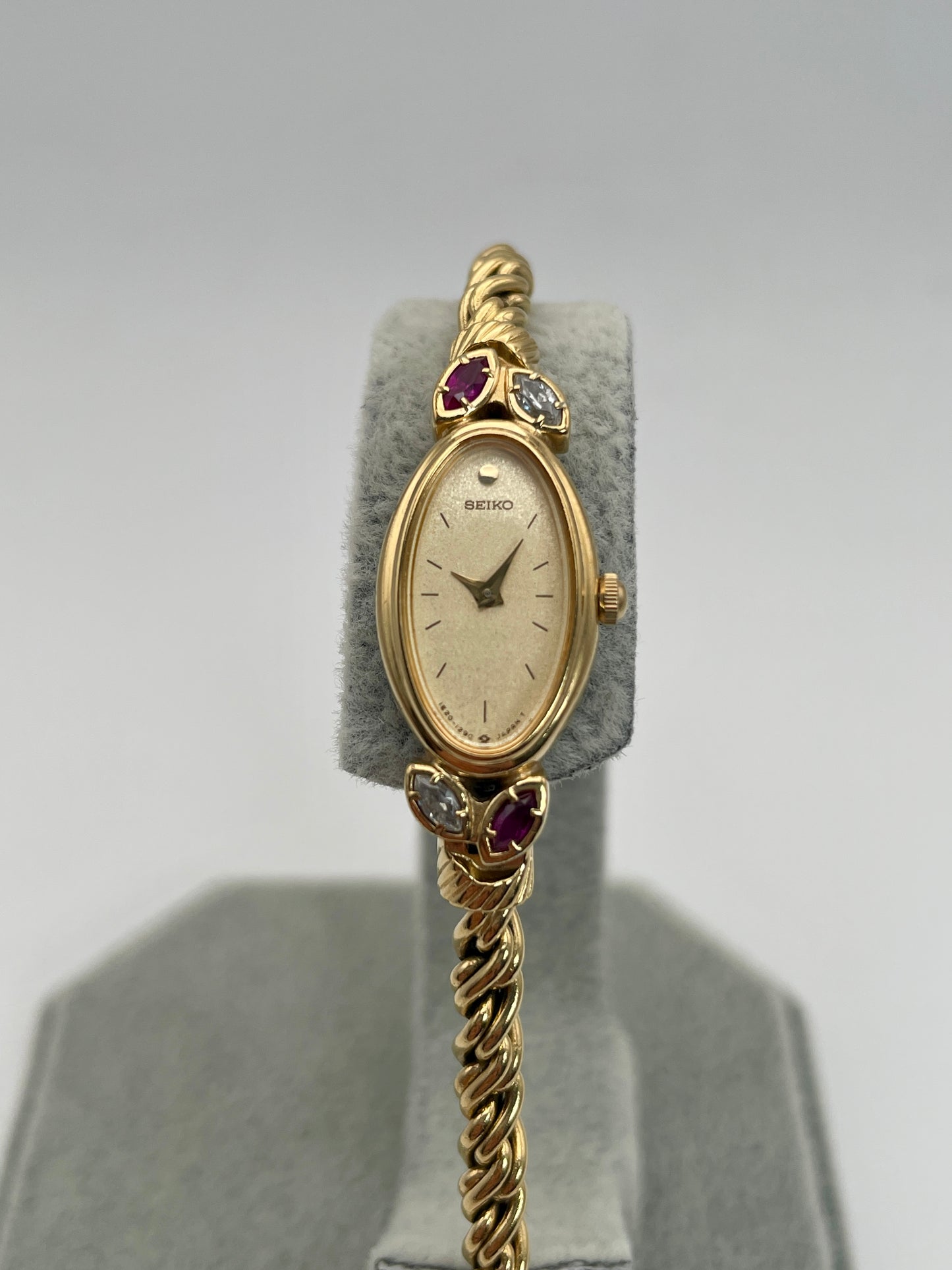 Front view of Seiko 1E20-5760 vintage women's watch in gold with ruby and diamond accents and twisted rope bracelet.