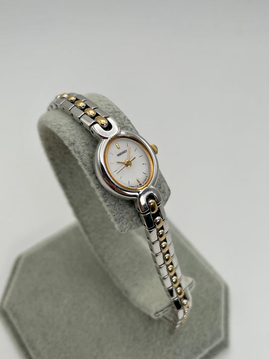 Seiko 1F21-5A40 two-tone watch on display stand, main view
