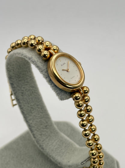 Diagonal left view of gold watch wit white face Seiko Alba Y588-5180 gold watch highlighting curved oval case and unique bracelet.