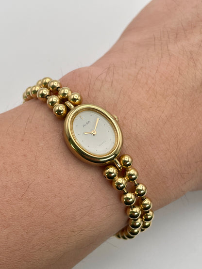 Gold wristwatch with beaded band on a wrist against a white background. Wrist shot view of Seiko Alba Y588-5180 women's watch showing bracelet fit and oval dial.