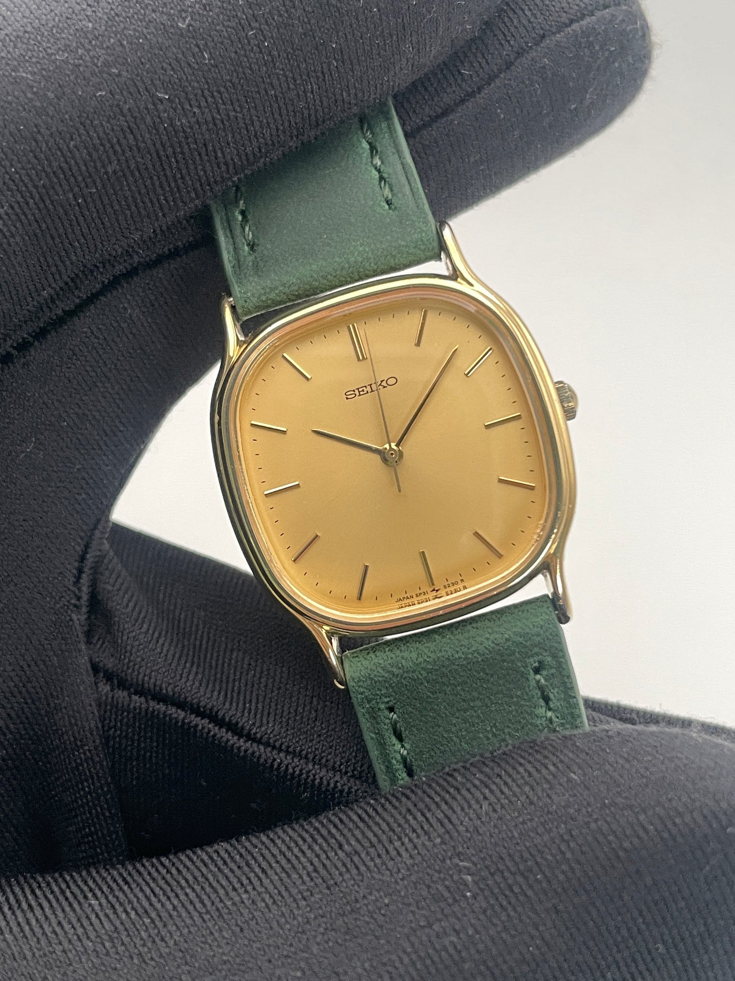 Close-up view of Seiko Chariot in gold-tone, showing minimalistic dial design with green leather strap.