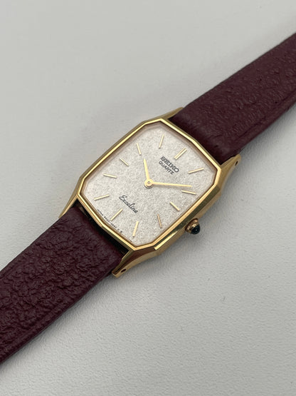 Angled view of Seiko Exceline Decagon Vintage Ladies Watch in gold-tone with textured silver dial and burgundy strap.