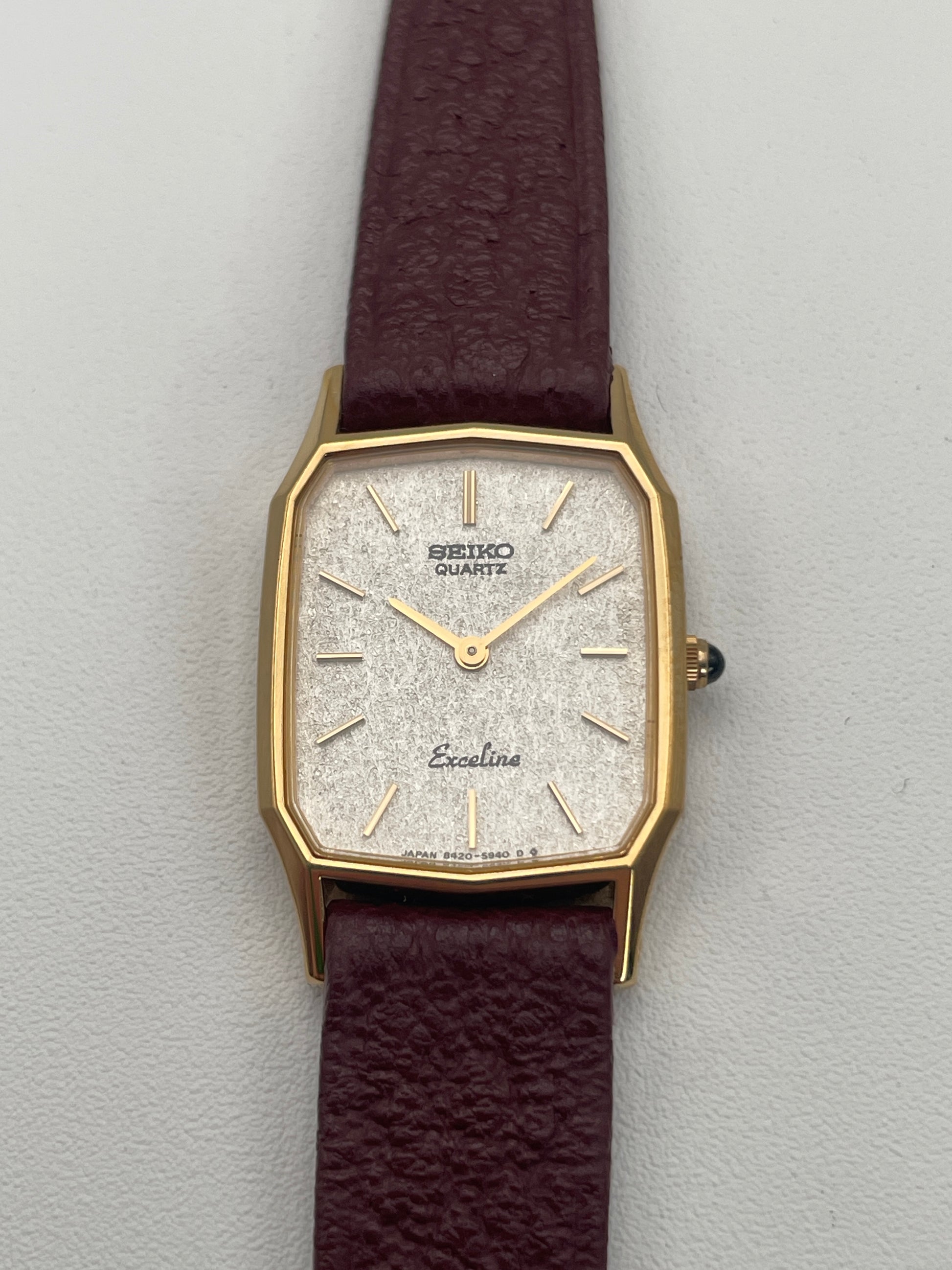 Seiko Exceline Decagon Ladies Watch in gold-tone case with silver textured dial, burgundy leather strap, photographed face forward.