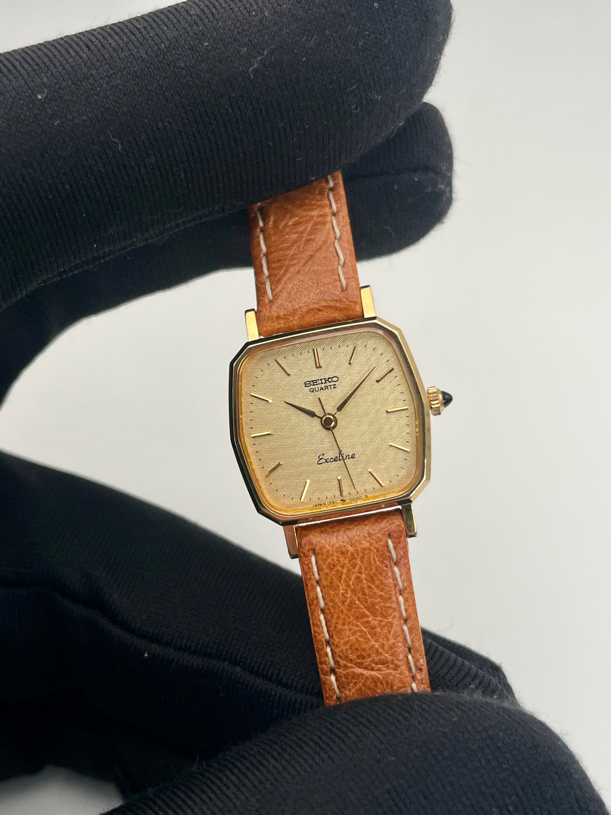 Handheld view of Seiko Exceline vintage women's watch in gold with tan leather strap, showcasing the octagonal case and elegant dial.