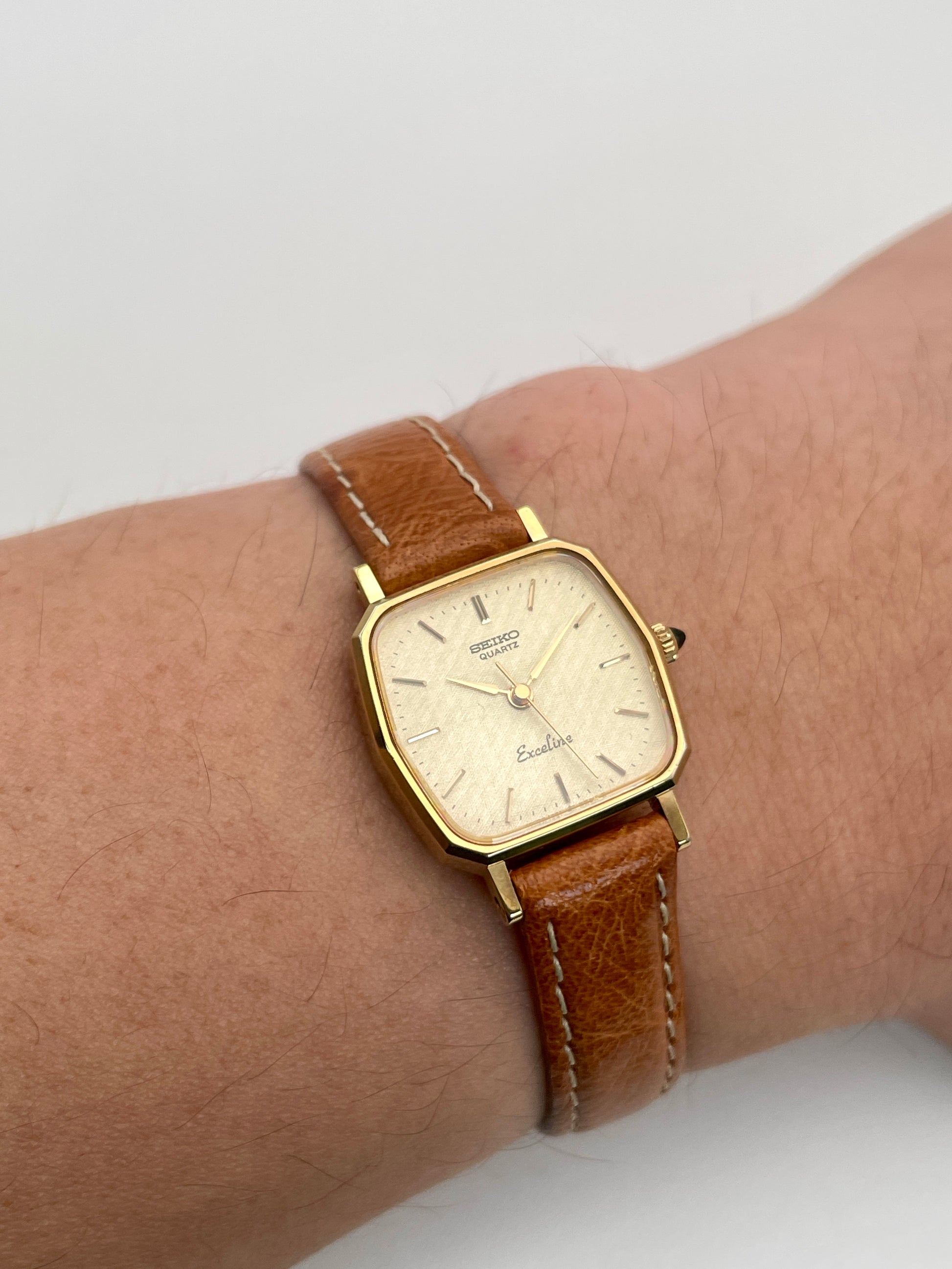 Wrist shot of Seiko Exceline vintage women's watch in gold with tan leather strap, highlighting the octagonal case shape and classic design.