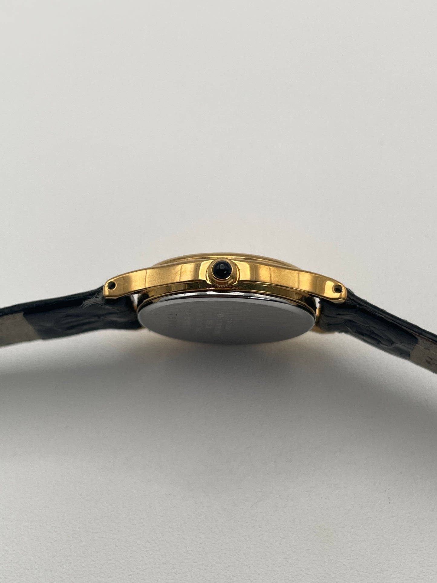 Side view of Seiko Exceline gold watch showing the gold crown with cabochon gem with a black leather strap and textured dial.