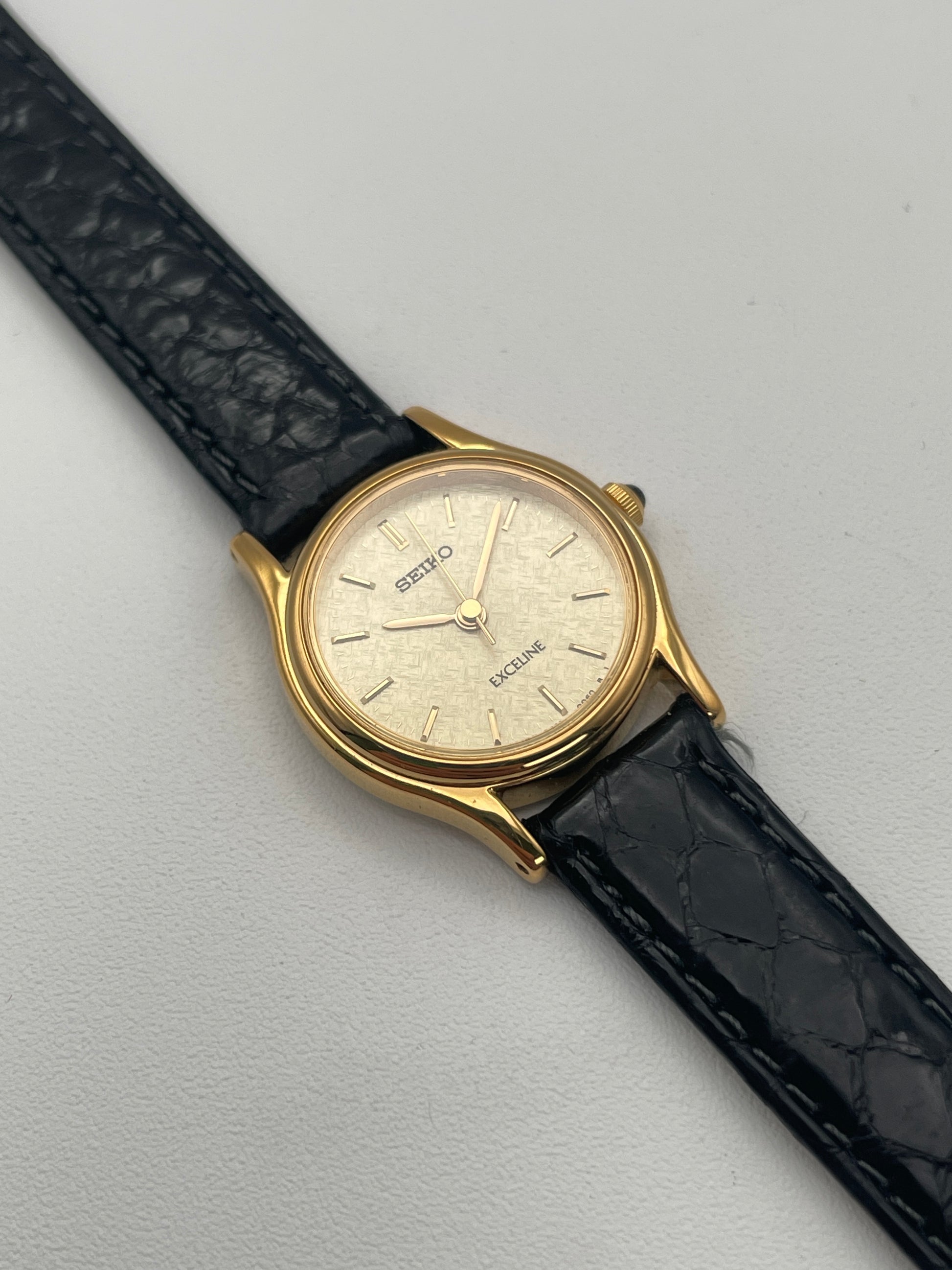 Front view of Seiko Exceline Ladies Watch in gold with a textured dial and black leather strap.