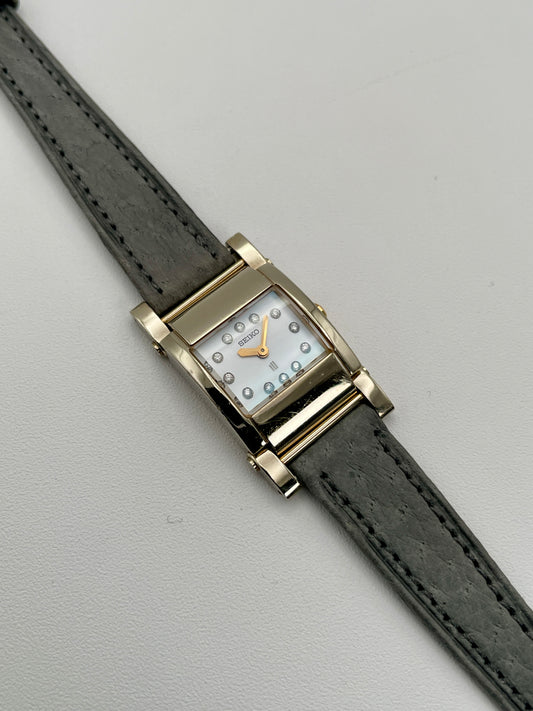 Front view of Seiko Lukia 1E20-0AH0 vintage women's watch in gold case, silver dial, and grey strap
