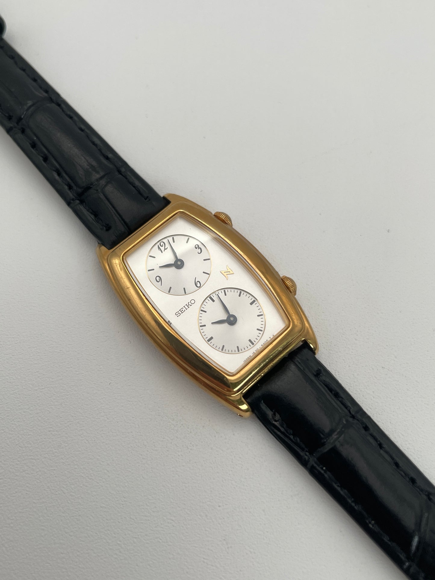 Seiko Noie Dual Time watch with a gold-tone rectangular case, dual dials, and black leather strap.