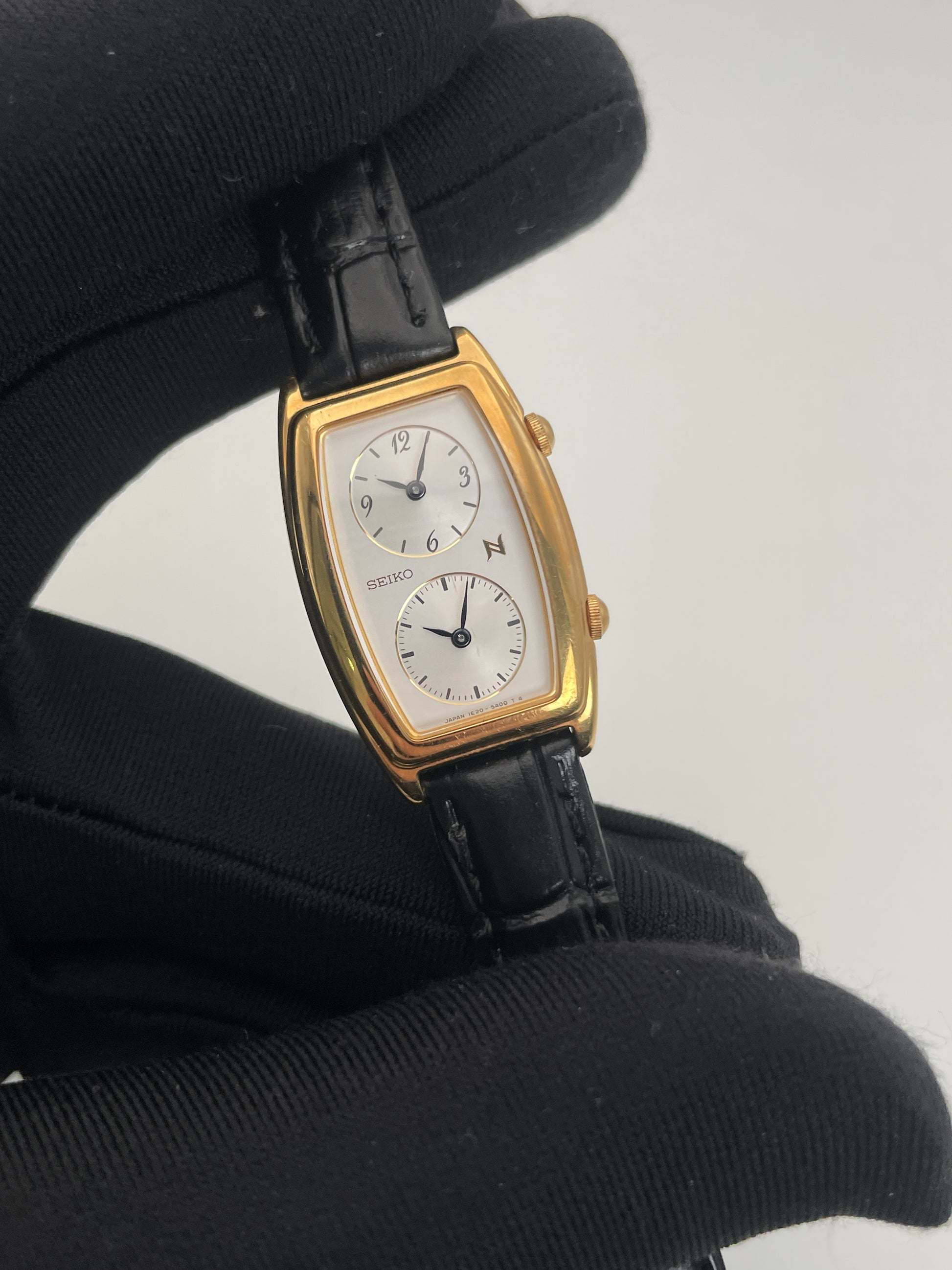 Close-up view of Seiko Noie Dual Time watch with a gold-tone rectangular case, dual dials, and black leather strap.
