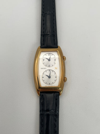 Front view of Seiko Noie Dual Time watch featuring a gold-tone rectangular case, dual dials, and black leather strap.