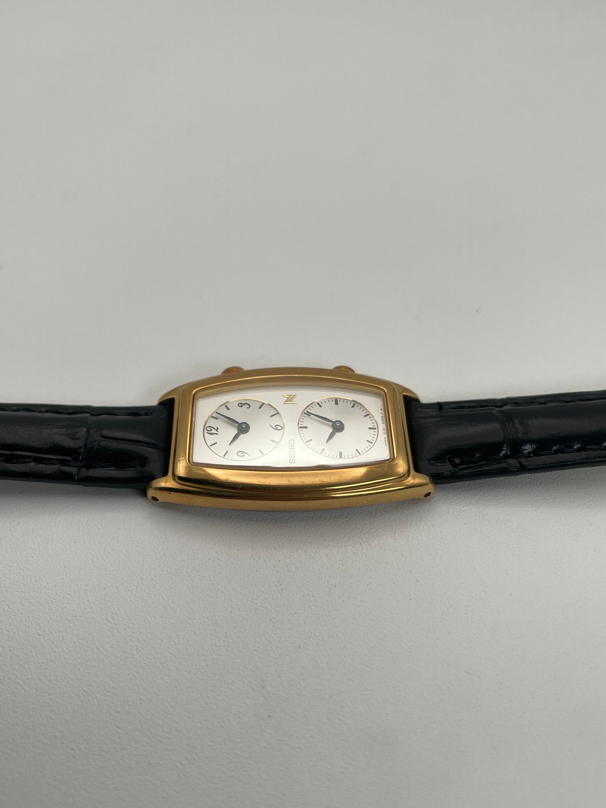 Side view of Seiko Noie Dual Time watch highlighting the gold-tone rectangular case and black leather strap.