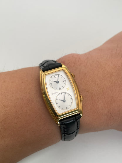 Seiko Noie Dual Time watch worn on wrist, featuring gold-tone rectangular case, dual dials, and black leather strap.