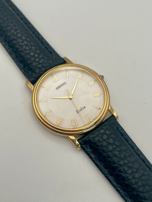 Front view of Seiko Dolce 8N41-7030 Vintage Watch in gold with black leather strap and white Roman numeral dial.