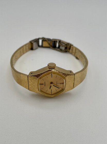 Flat lay angled view of a vintage Seiko ladies' watch, displaying its gold-tone textured case, bracelet, and minimalist gold dial with black hour markers and hands.