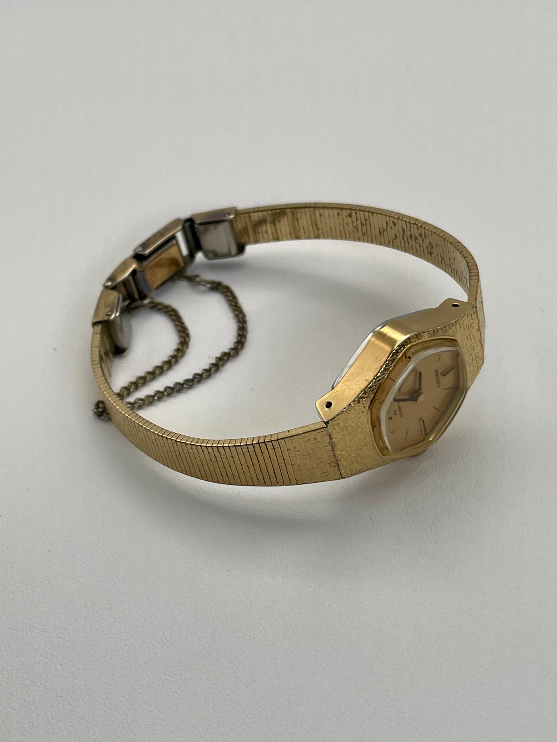 Flat lay angled view of a vintage Seiko ladies' watch, displaying its gold-tone textured case, bracelet, and minimalist gold dial with black hour markers and hands.