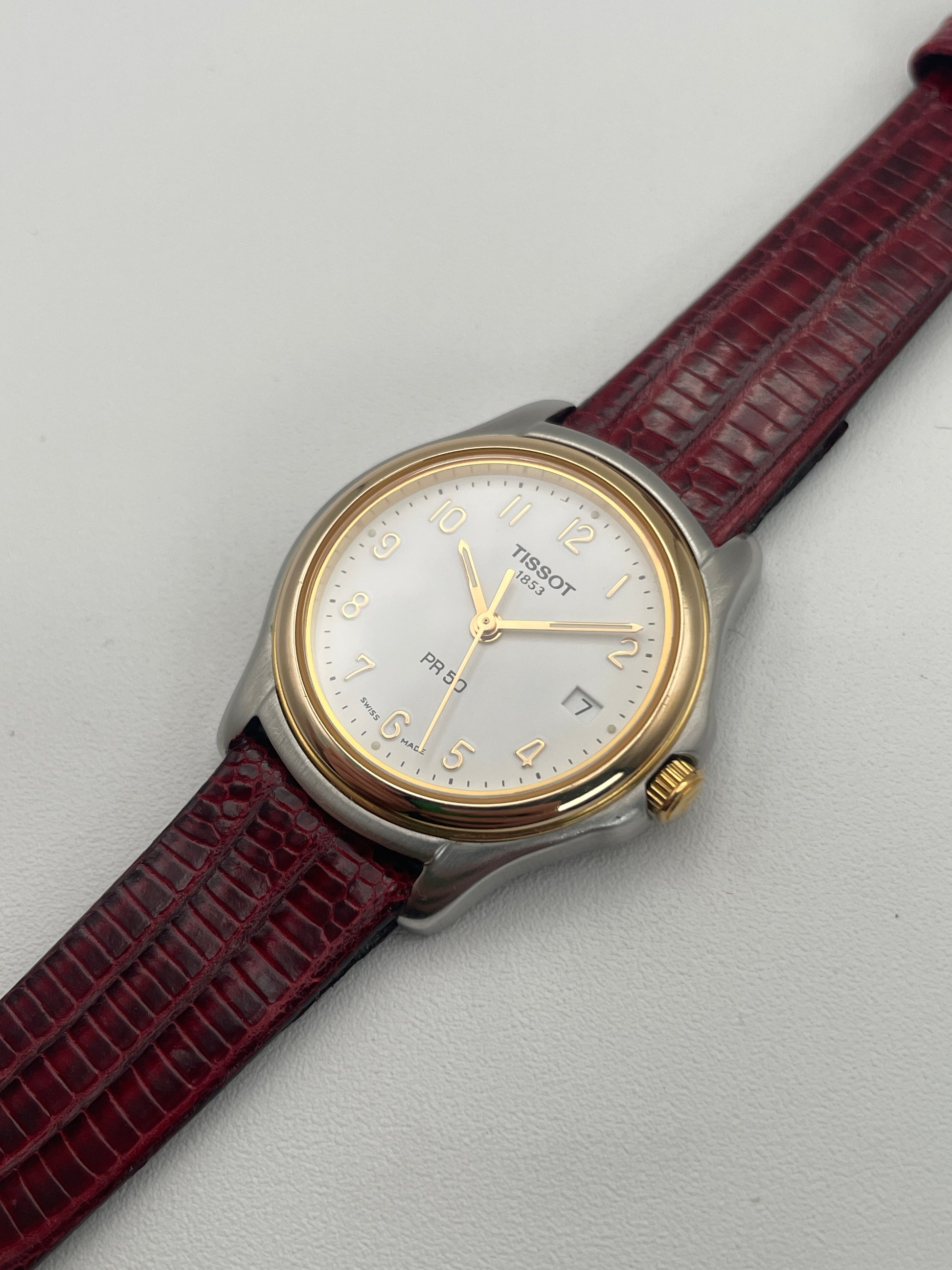 Diagonal view of Tissot PR50 watch, highlighting gold bezel and red leather strap.