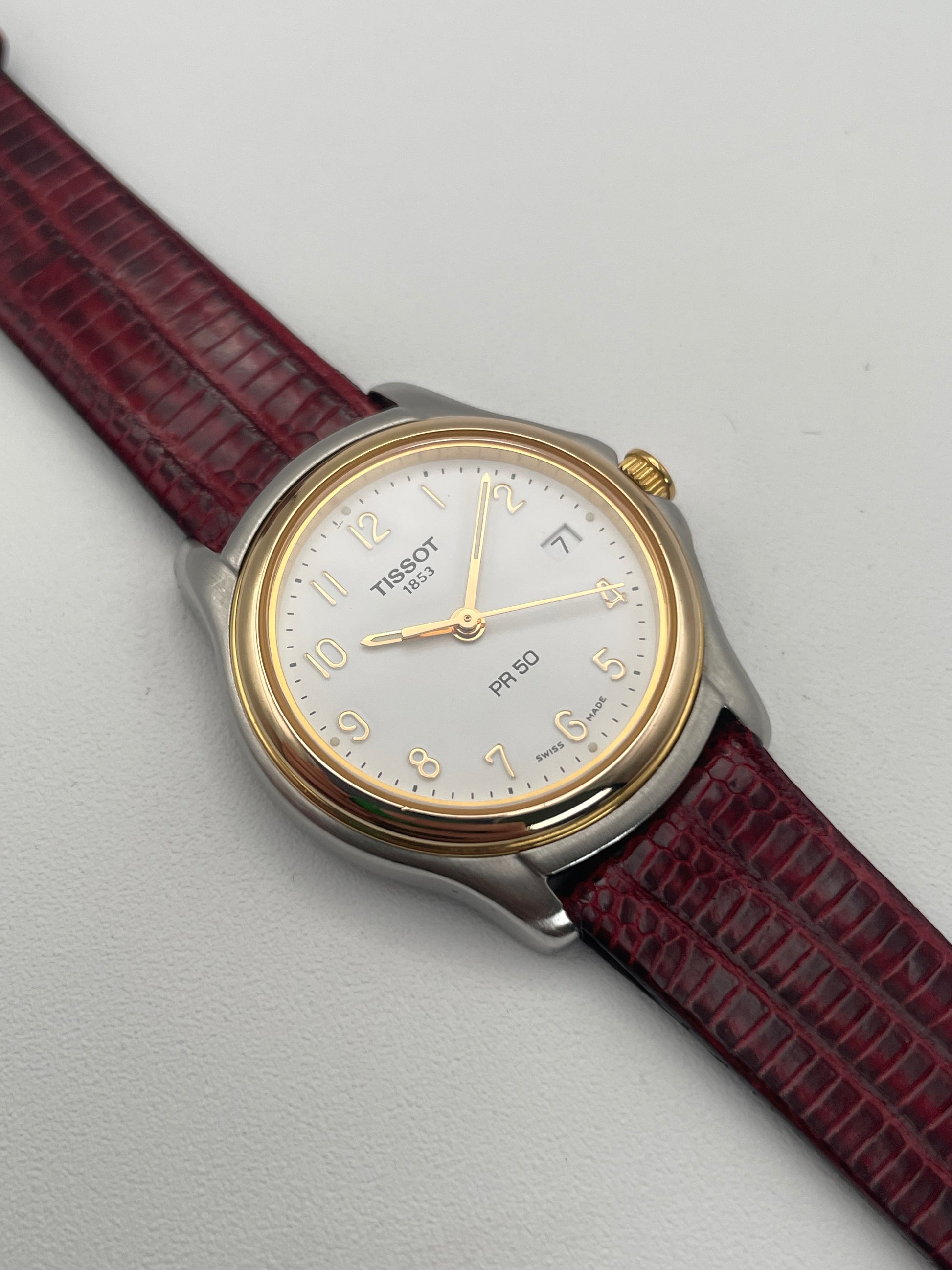 View of Tissot PR50 gold and stainless steel vintage watch with red leather strap.