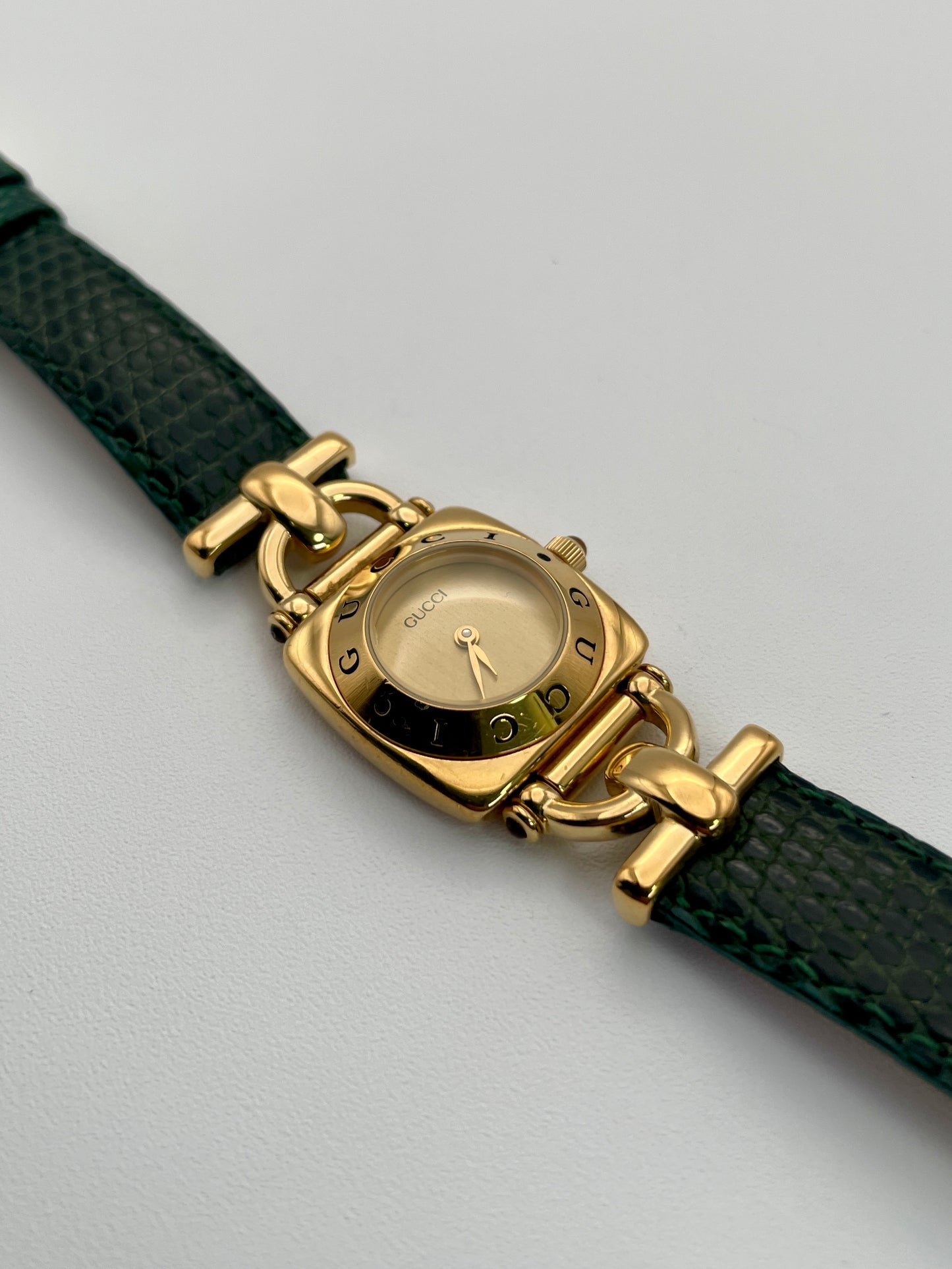 Gucci 6300L ladies' watch with a  gold square case, gold dial, and green lizard skin strap, showing the intricate design and logo.