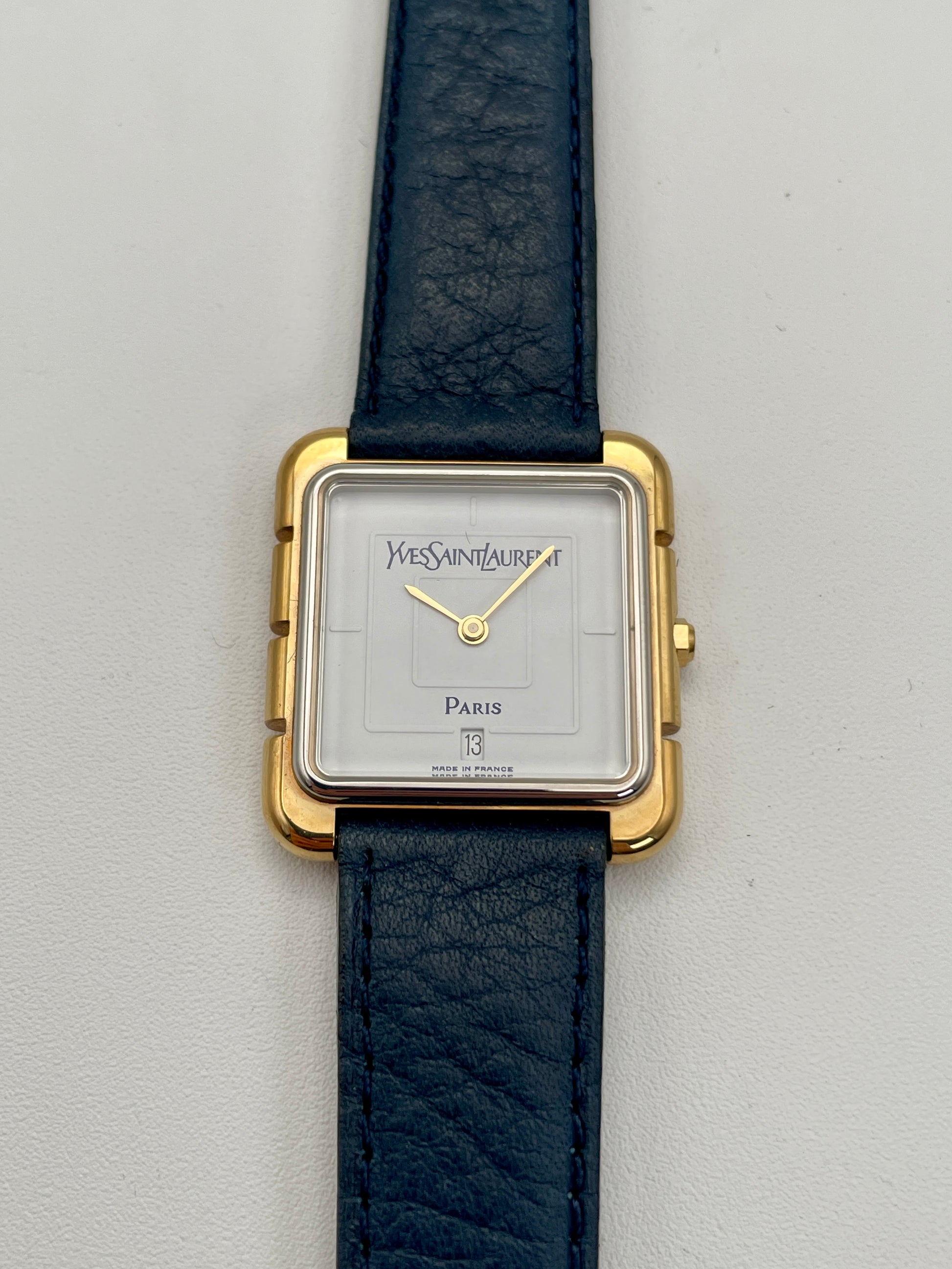 Front view of Yves Saint Laurent 3D Square watch with gold case, white dial, and blue leather strap.