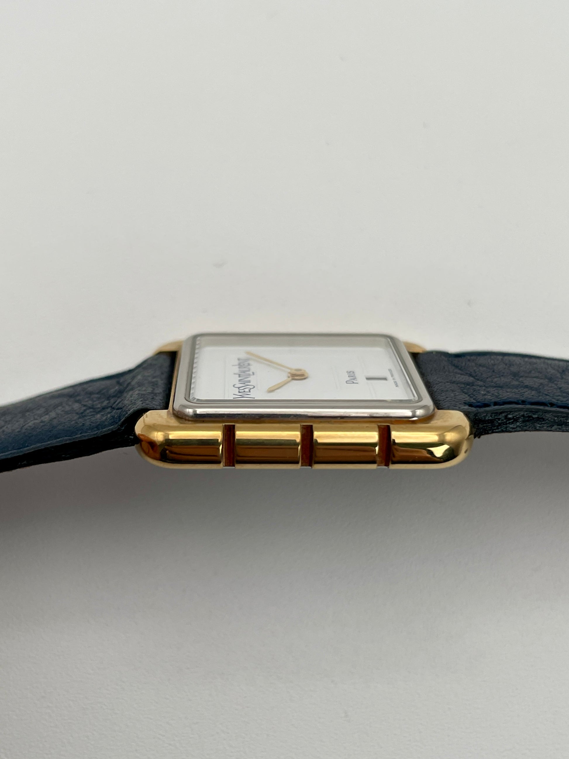 Side case view of Yves Saint Laurent 3D Square watch with gold case and blue leather strap.