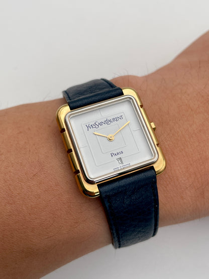 Wrist shot view of Yves Saint Laurent 3D Square watch with gold case, white dial, and blue leather strap.