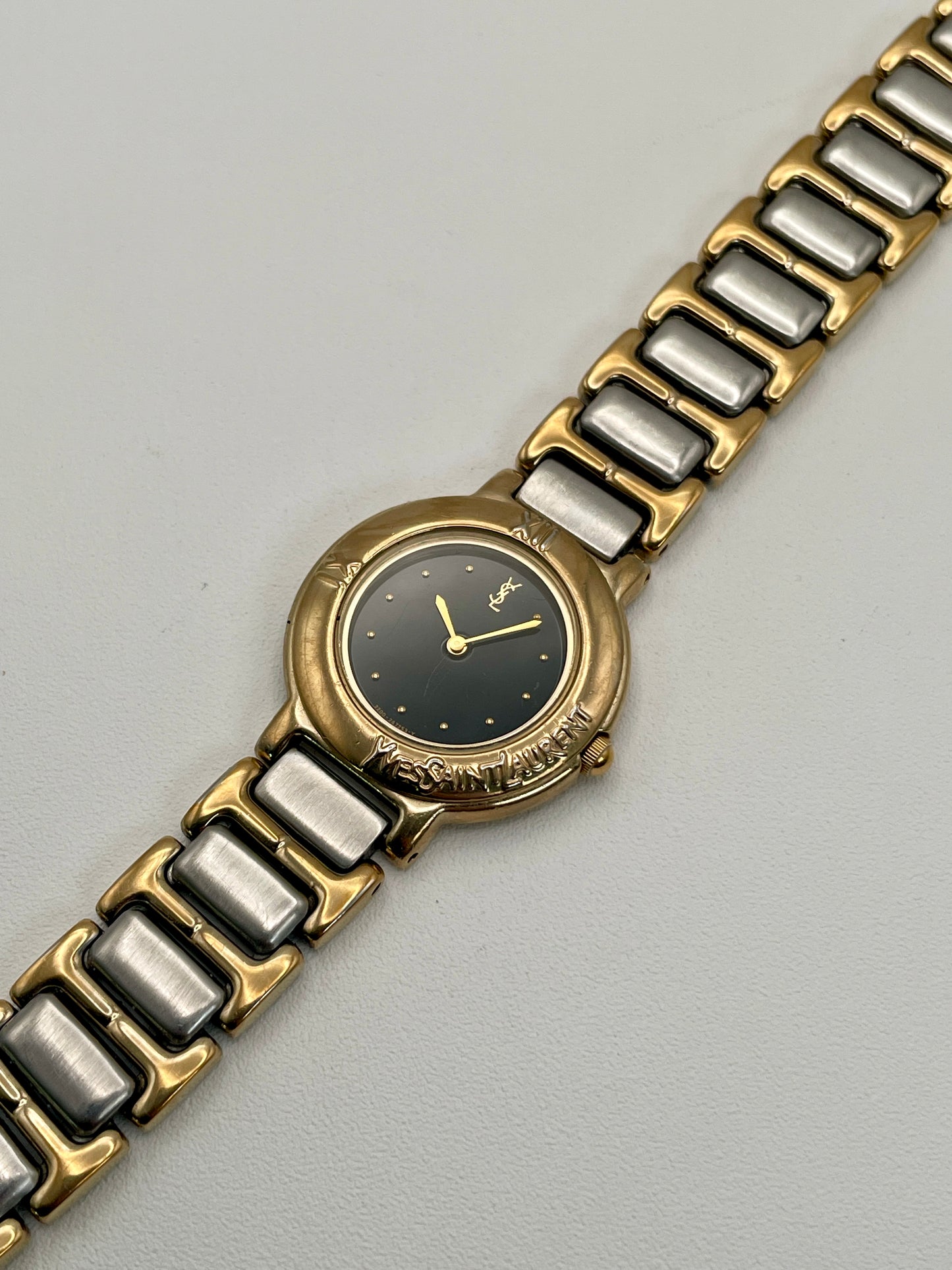 Diagonal close-up view of the YSL Black Pour Femme watch highlighting the dial, engraved bezel, and two-tone bracelet.