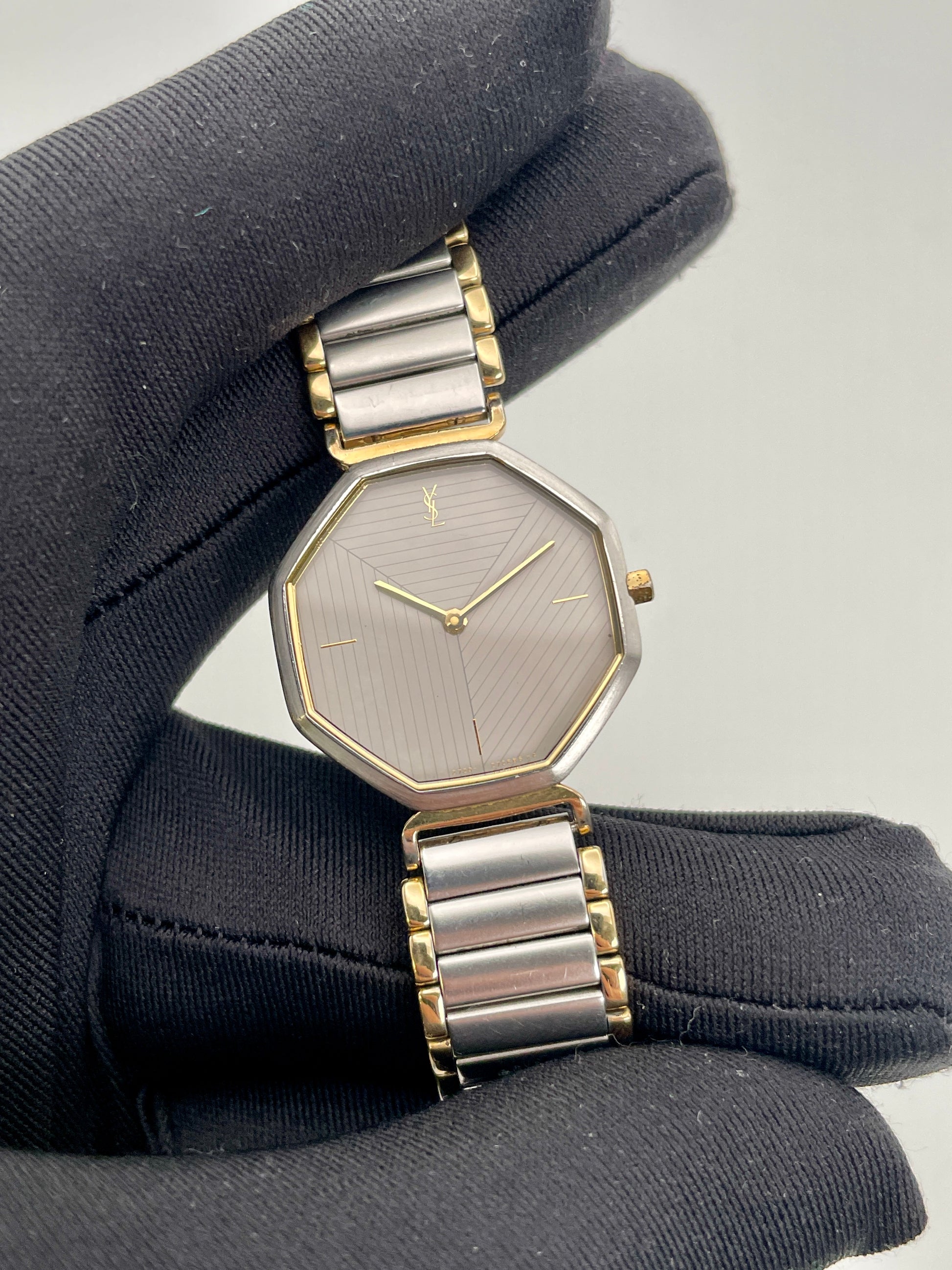 Close-up view of the YSL octagon watch held by glove, highlighting grey dial and gold hands
