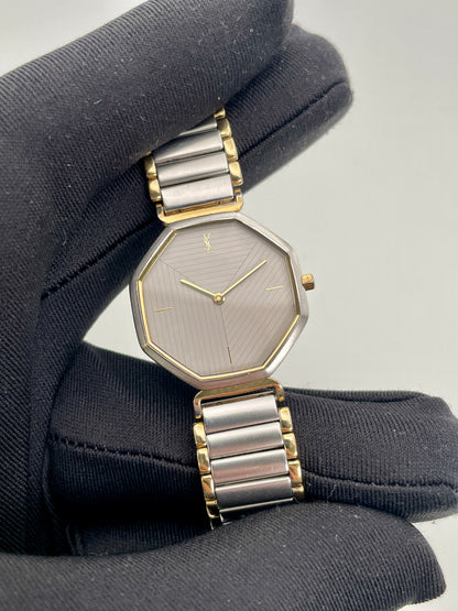 Close-up view of the YSL octagon watch held by glove, highlighting grey dial and gold hands
