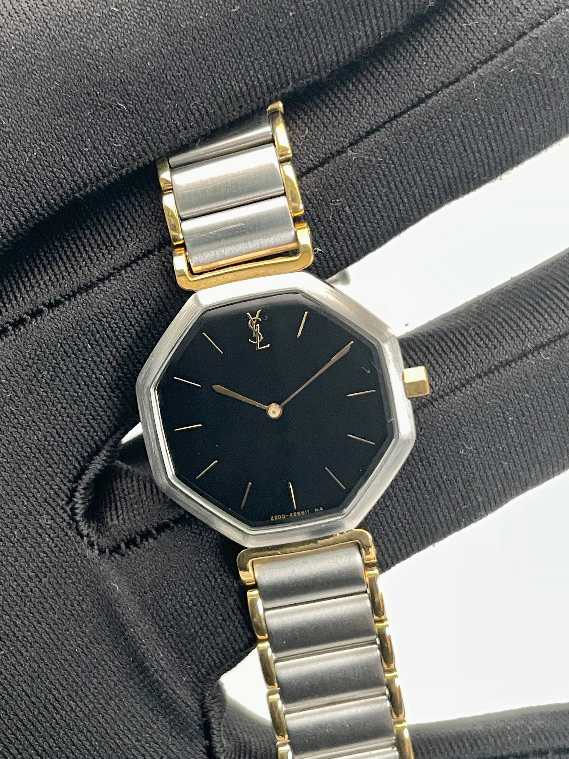 Handheld view of the Yves Saint Laurent Octagon Vintage Women's Watch showing its elegant two-tone bracelet and black dial.