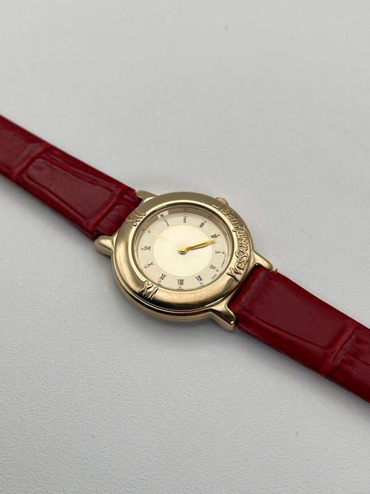 Yves Saint Laurent Pour Femme watch featuring a gold case, champagne dial, and a vibrant red leather strap.
