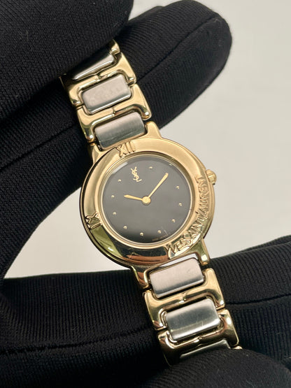 Close-up view of Yves Saint Laurent vintage ladies Pour Femme watch's black dial, gold hands, and two-tone bracelet.