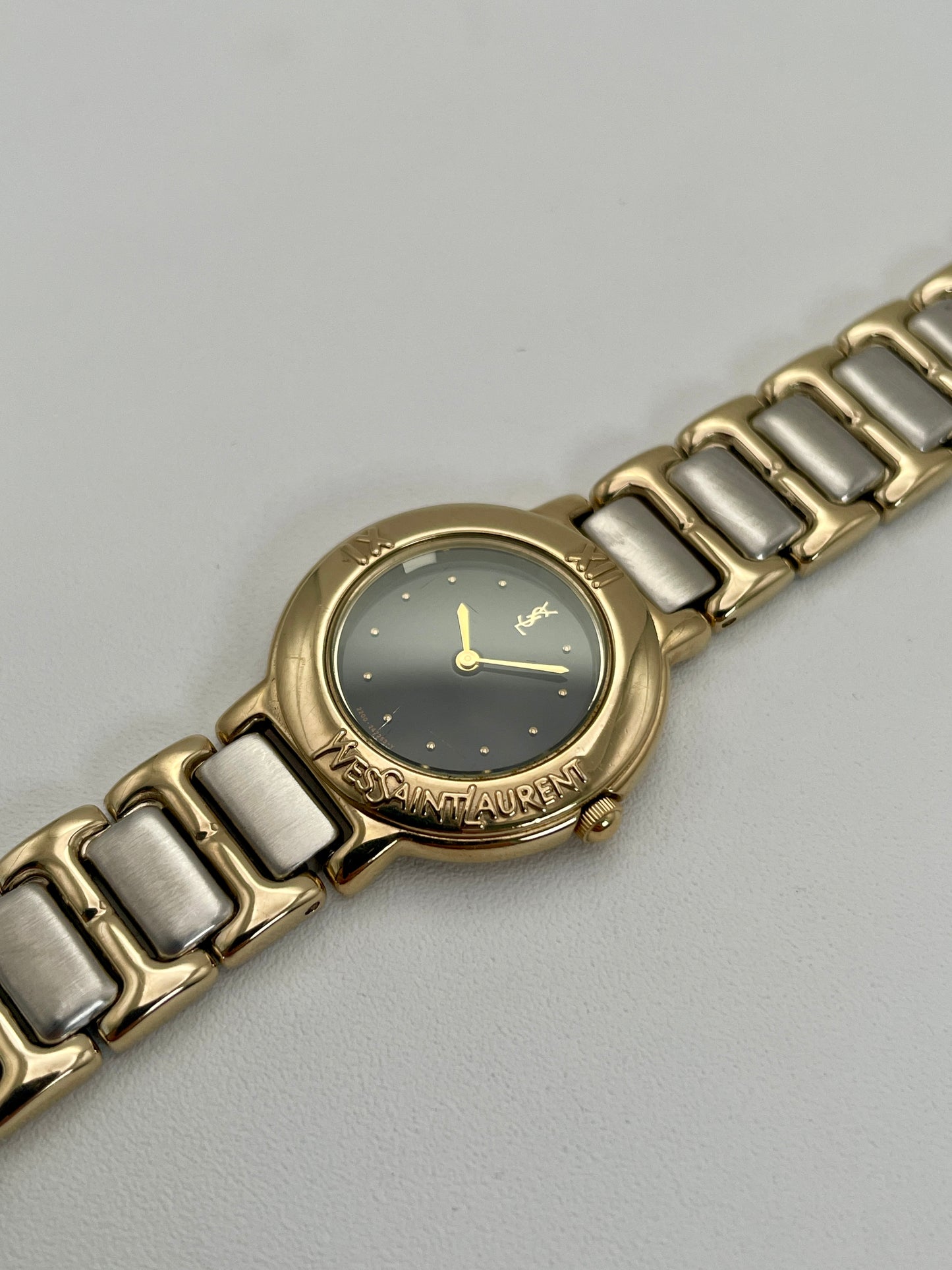 Diagonal view of Yves Saint Laurent Pour Femme watch with gold case, black dial, and two-tone bracelet