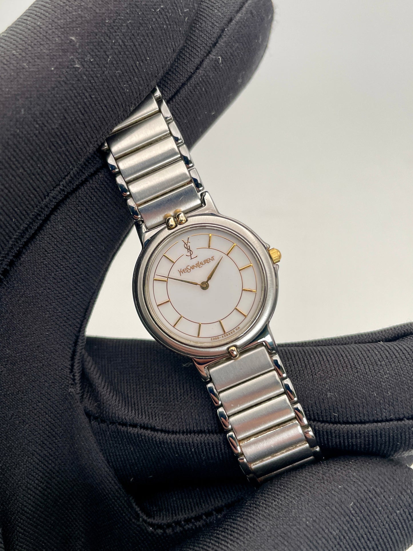 Close-up view of the vintage Yves Saint Laurent two-tone watch, focusing on the stainless steel and gilt case and white dial.