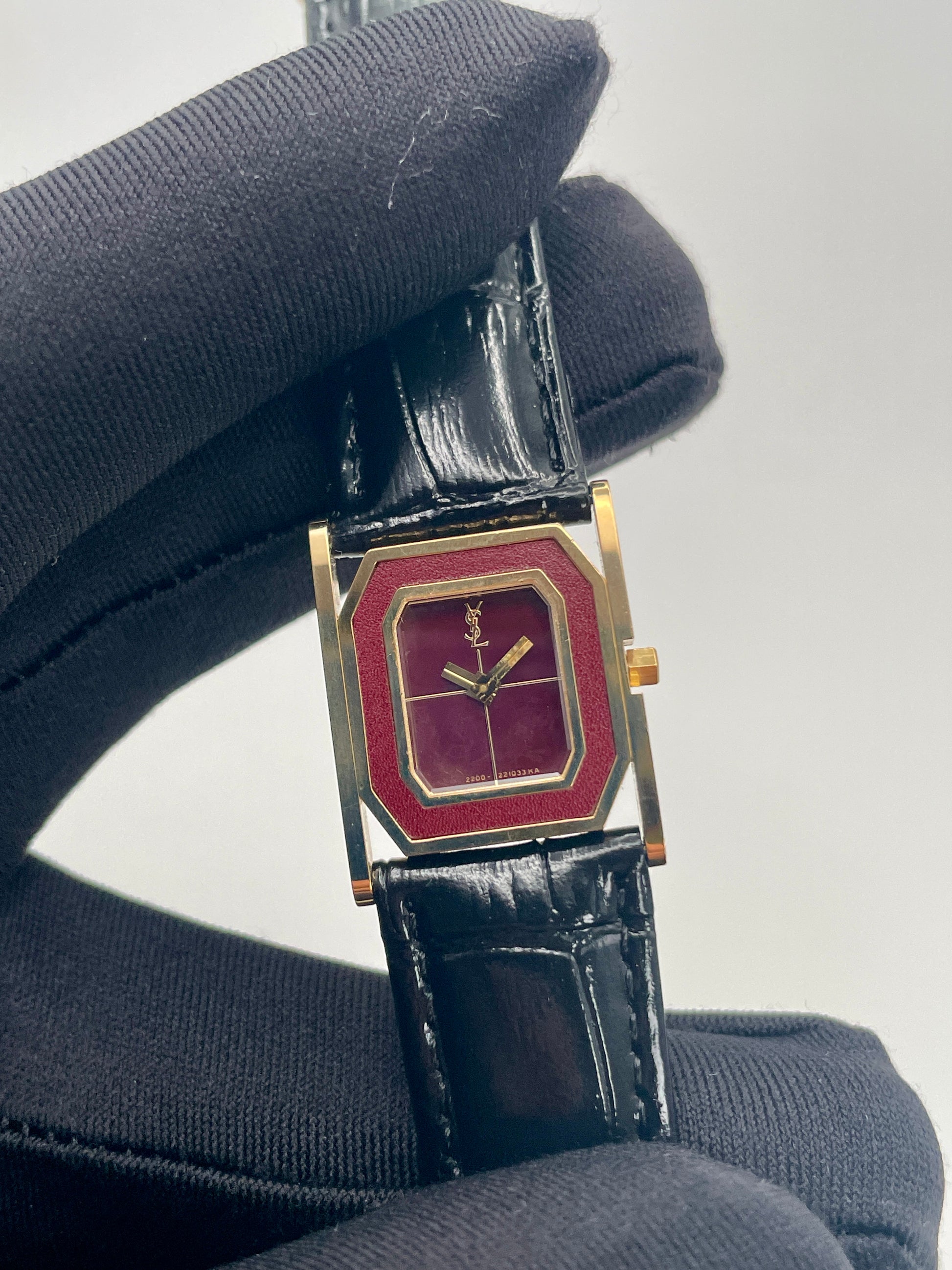 Close-up of the YSL Tank watch highlighting the burgundy dial, gold case, and logo