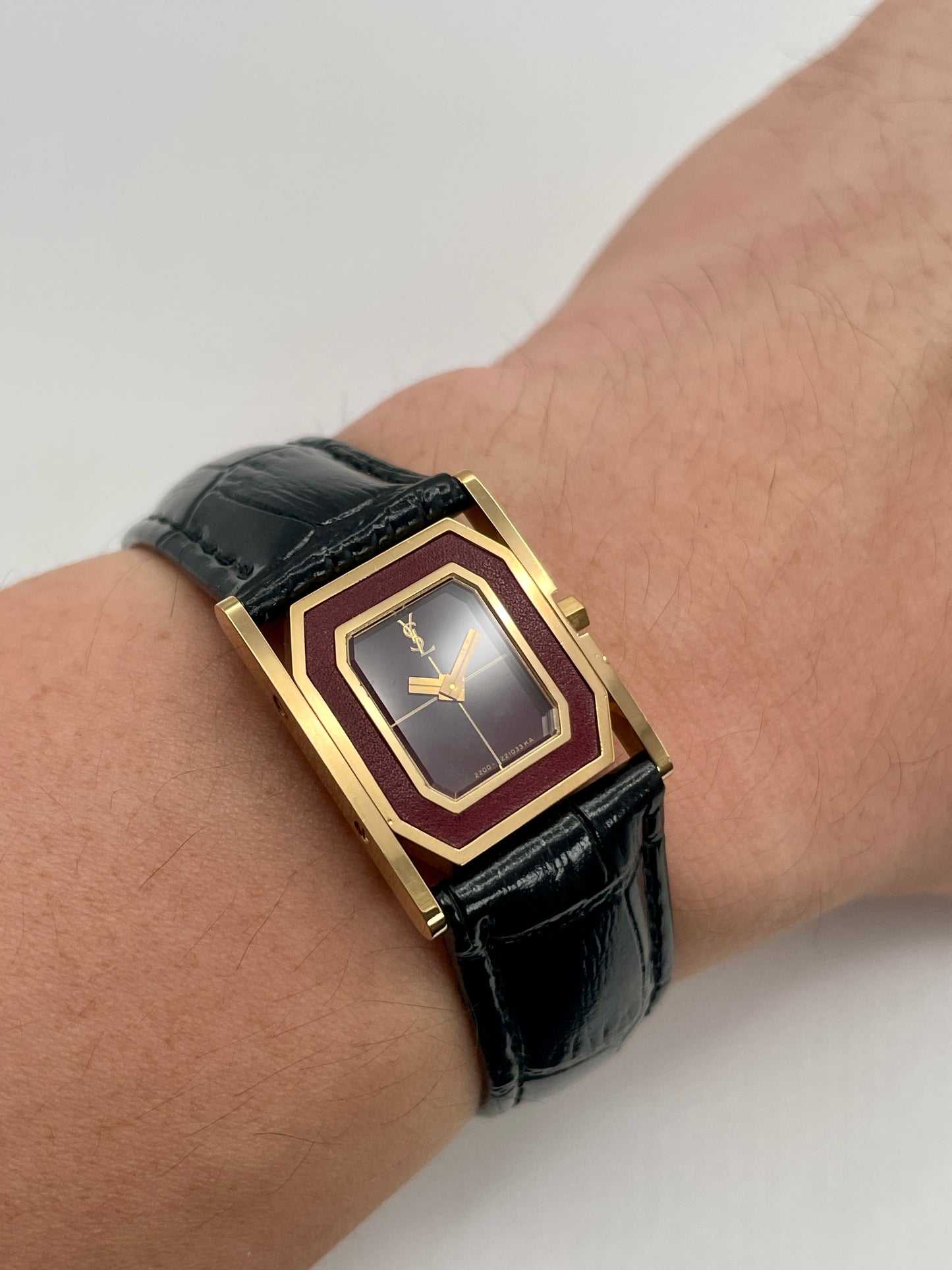 Wrist shot of the Yves Saint Laurent Tank gold watch with burgundy dial and black strap