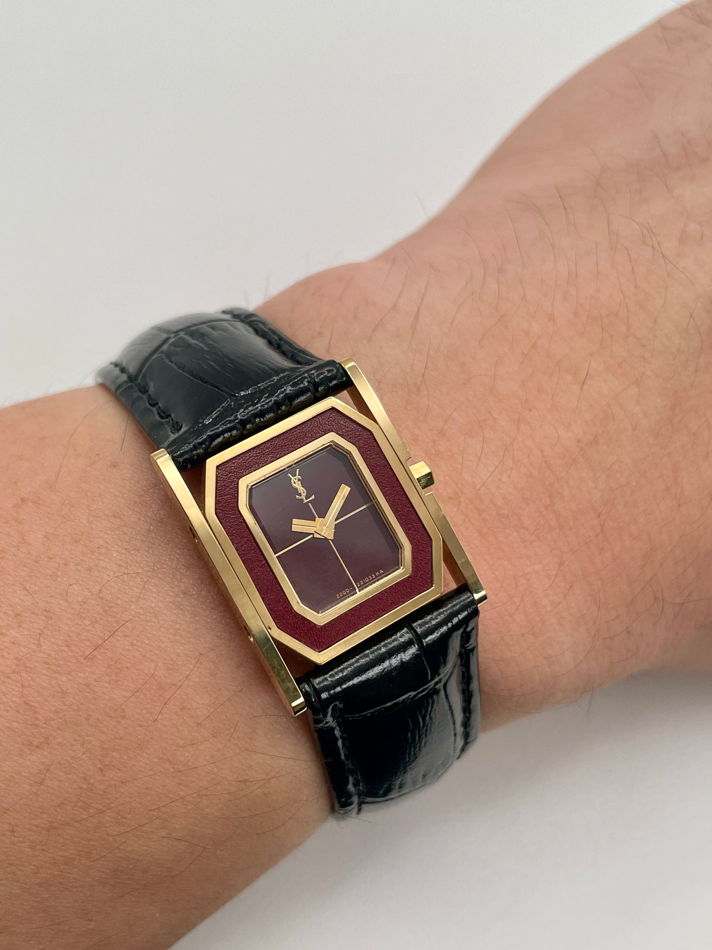 Wrist shot of the Yves Saint Laurent Tank gold watch with burgundy dial and black strap