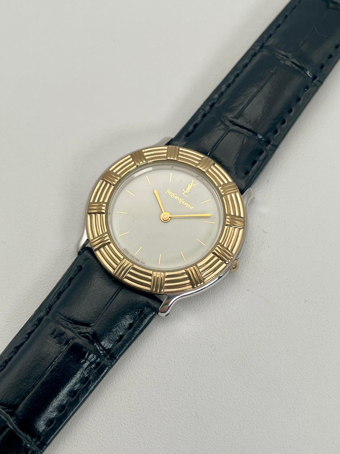 Angle view of Yves Saint Laurent vintage watch with a gold bezel and black leather strap.
