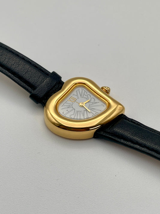 ront view of a Yves Saint Laurent Heart vintage gold watch with a curved case, white dial, Roman numerals, and black leather strap.